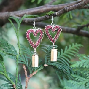 Handmade chainmail heart earrings in red and silver hanging from a cedar branch. The earrings feature upcycled 9mm brass bullet casings dangling from the bottom, symbolizing spiritual alchemy and transformation.